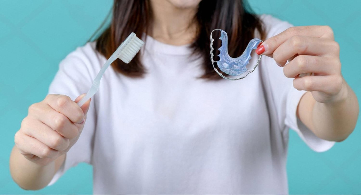 Patient cleaning a Hawley retainer with a toothbrush, showing daily retainer care